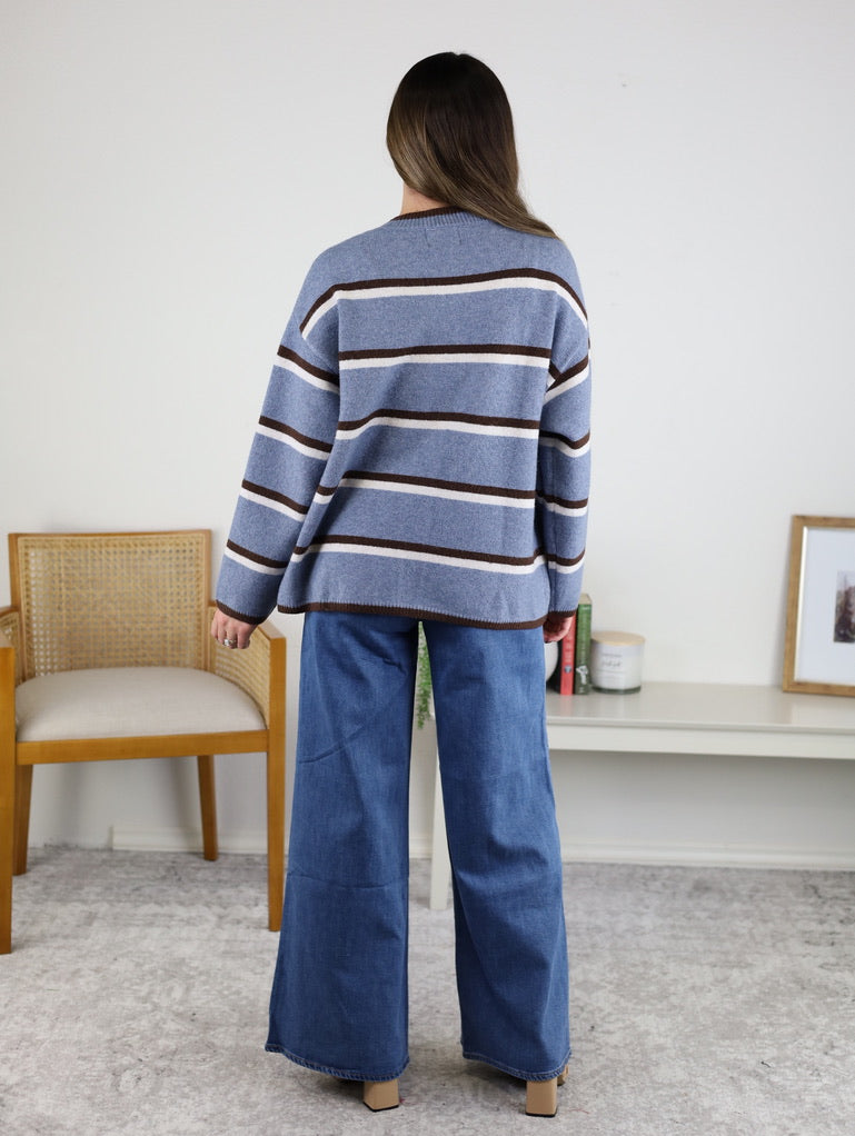 A person seen from behind wearing a blue, white, and brown Nora Stripe Button Down Knit Cardigan with relaxed-fit blue jeans.