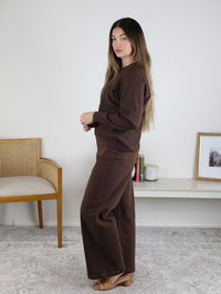 A person wearing a dark brown, round-neck viscose blend Eli Front Seam Sweater with a front seam and matching brown wide-leg pants.