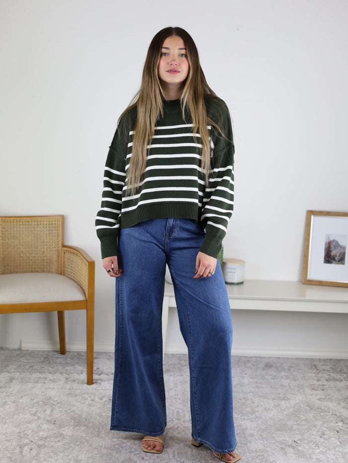 A person wearing a forest green and white striped Noa Striped Sweater in a cotton knit paired with wide-leg blue jeans.
