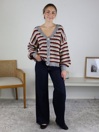 A woman wears the Grayson Relaxed Stripe V-Neck Button Cardigan in burgundy, cream, and grey with wide-leg dark wash jeans as a fall wardrobe staple.
