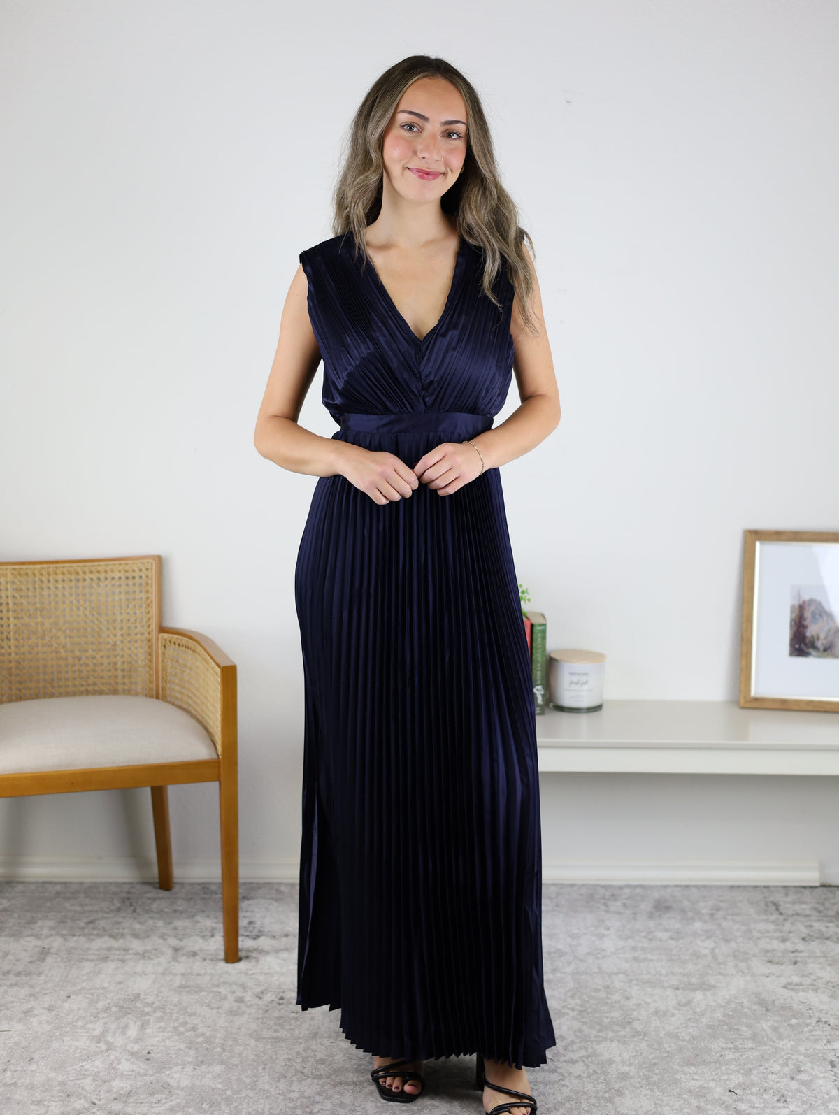 A woman wearing a navy blue Petal Pleated Satin V Neck Maxi Dress, featuring a sleeveless design and pleated satin fabric.