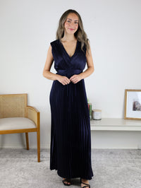 A woman wearing a navy blue Petal Pleated Satin V Neck Maxi Dress, featuring a sleeveless design and pleated satin fabric.