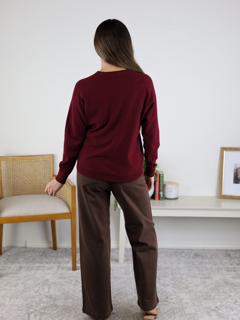 A person viewed from the back wearing the Eli Front Seam Sweater in burgundy with a round neck and brown trousers.