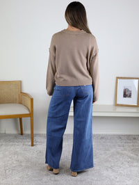 A person wearing a tan Jude Raw Edge Cardigan and wide-leg blue jeans.