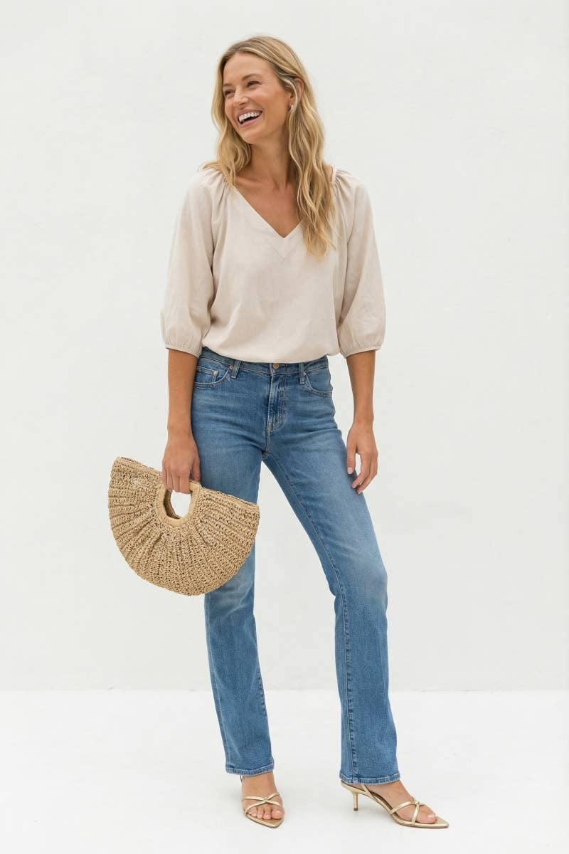 A woman wearing a Naked Zebra - Elastic Puff Sleeve V-neck Blouse: Burgundy / L and blue jeans, carrying a woven semicircular handbag.
