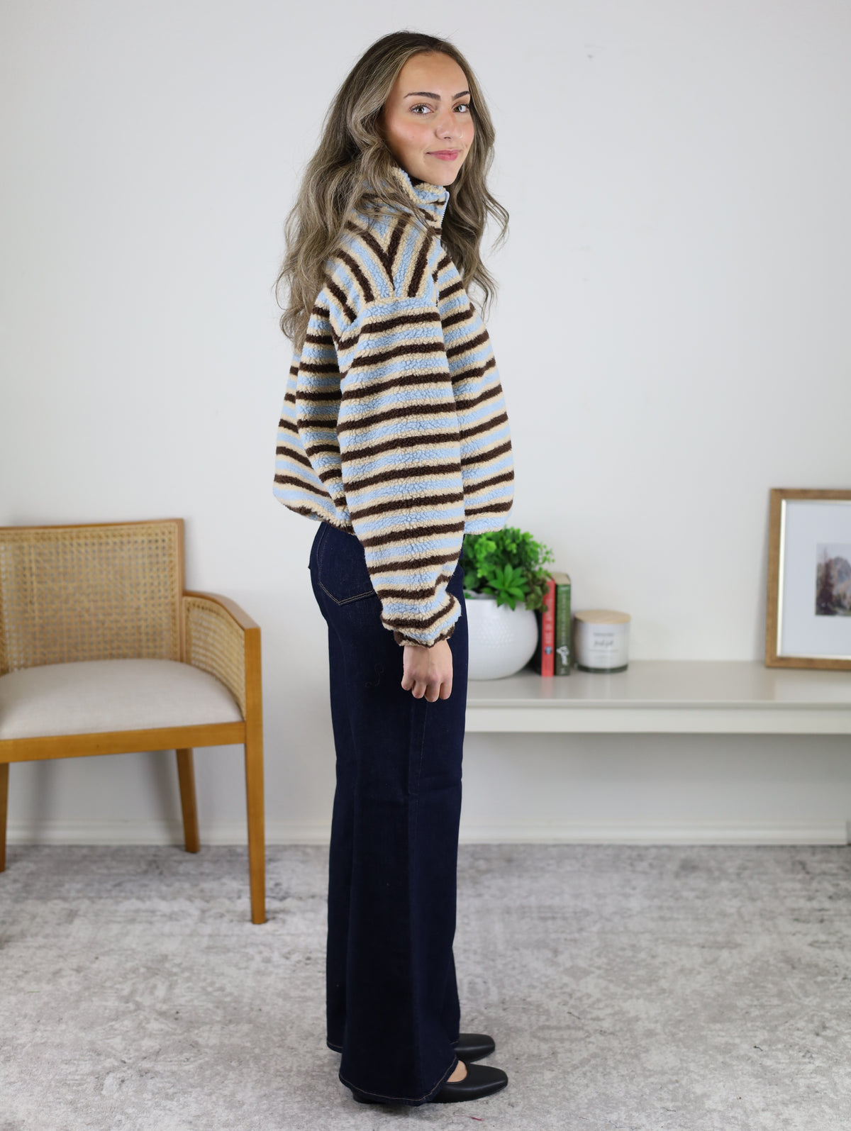A person wearing a cozy, coastal-inspired Coastal Stripe Sherpa Striped Half Zip Pullover with blue and brown stripes paired with dark blue jeans.