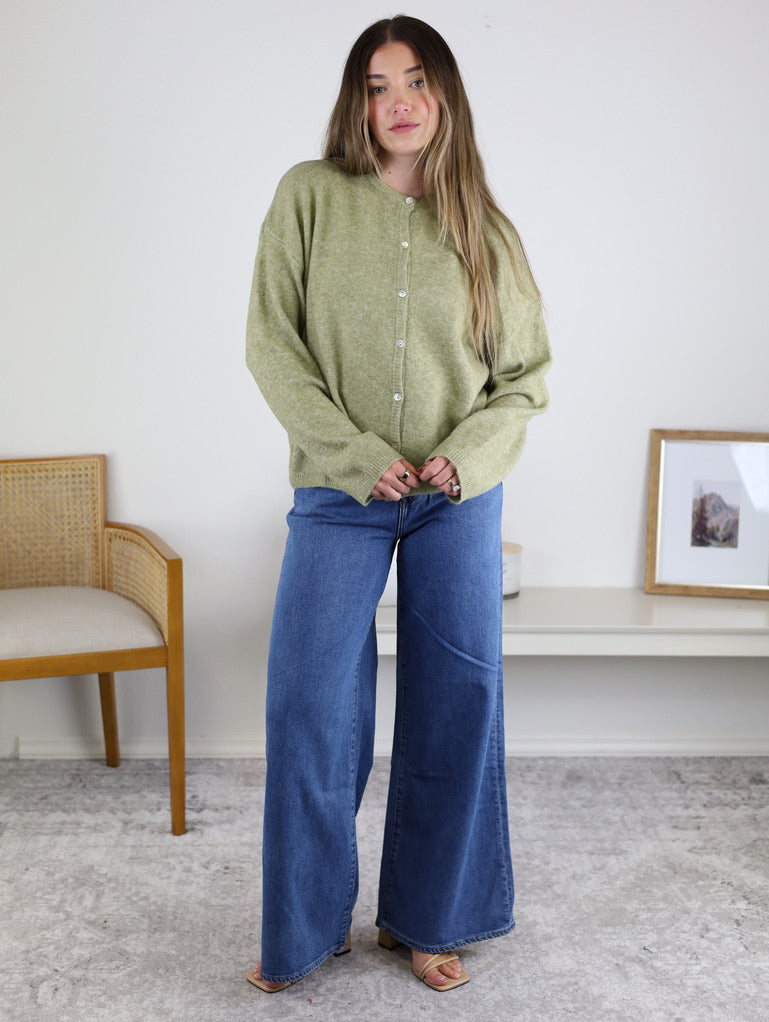 A person wearing an Olive Oversized Cardigan in sage green with wide-leg blue jeans.