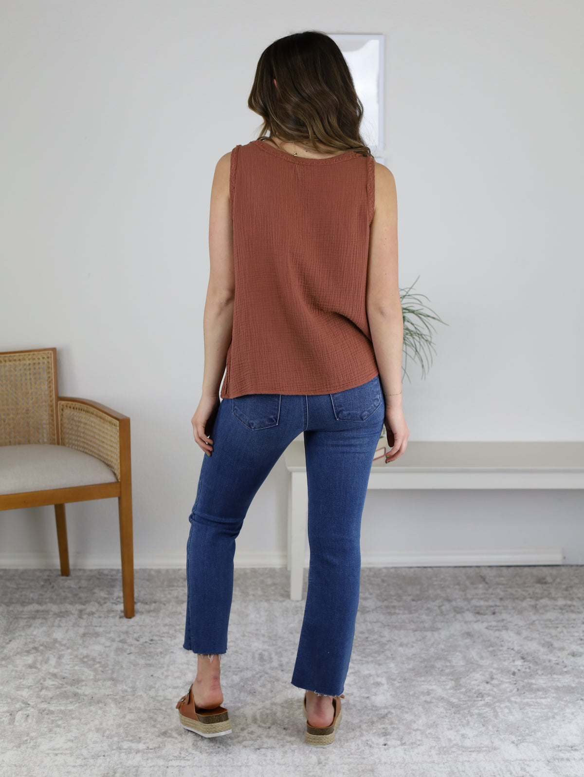 A person viewed from behind wearing a rust-colored sleeveless top and High Rise Tonal Crop Flare Denim with raw hems, paired with tan platform sandals.