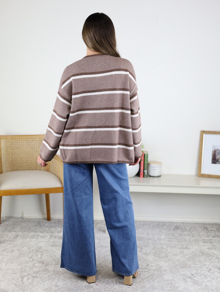 A person seen from behind wears a brown Nora Stripe Button Down Knit Cardigan with white horizontal stripes and wide-leg blue jeans.