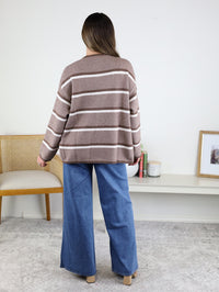 A person seen from behind wears a brown Nora Stripe Button Down Knit Cardigan with white horizontal stripes and wide-leg blue jeans.