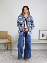 A woman wearing a blue and brown striped Nora Stripe Button Down Knit Cardigan over a white shirt and wide-leg blue jeans.