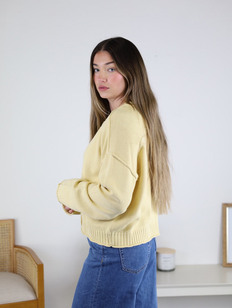 A woman wearing a pale yellow Jude Raw Edge Cardigan with raw edge detailing and blue jeans.