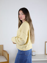 A woman wearing a pale yellow Jude Raw Edge Cardigan with raw edge detailing and blue jeans.