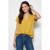 A woman wearing a mustard yellow, short-sleeved, drop-shoulder Naked Zebra - Drop Shoulder Regular Blouse: Chocolate / L with a V-neckline and blue jeans.