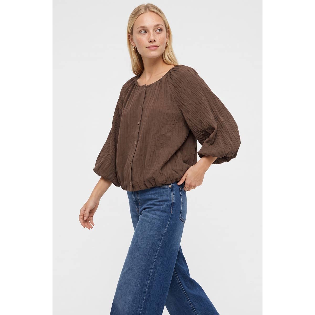 A black Naked Zebra - Crinkle Texture Bubble Hem Button Up Blouse with a crinkle texture, a rounded neckline, and a gathered bubble hem worn with blue jeans.