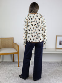 A person wearing a cozy, cream-colored floral print Casin Floral Print Fluffy Fleece Jacket with brown trim and dark blue wide-leg jeans.