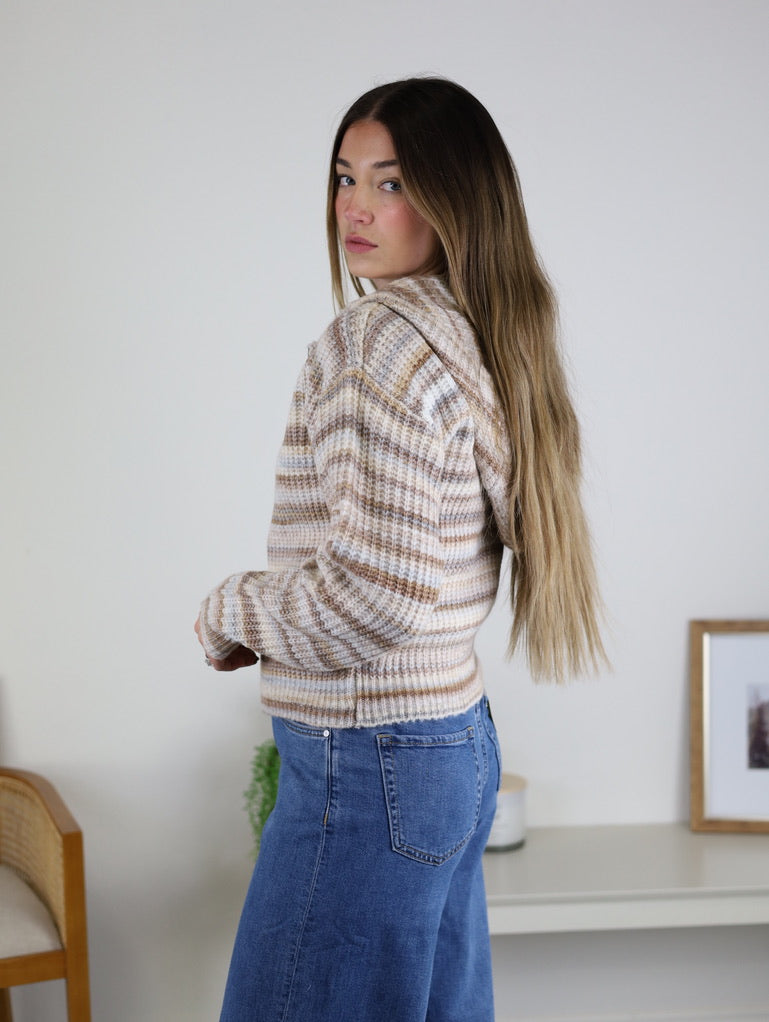 A person wearing a cozy, striped zip-front Romy Hooded Cardigan Sweater and blue jeans.