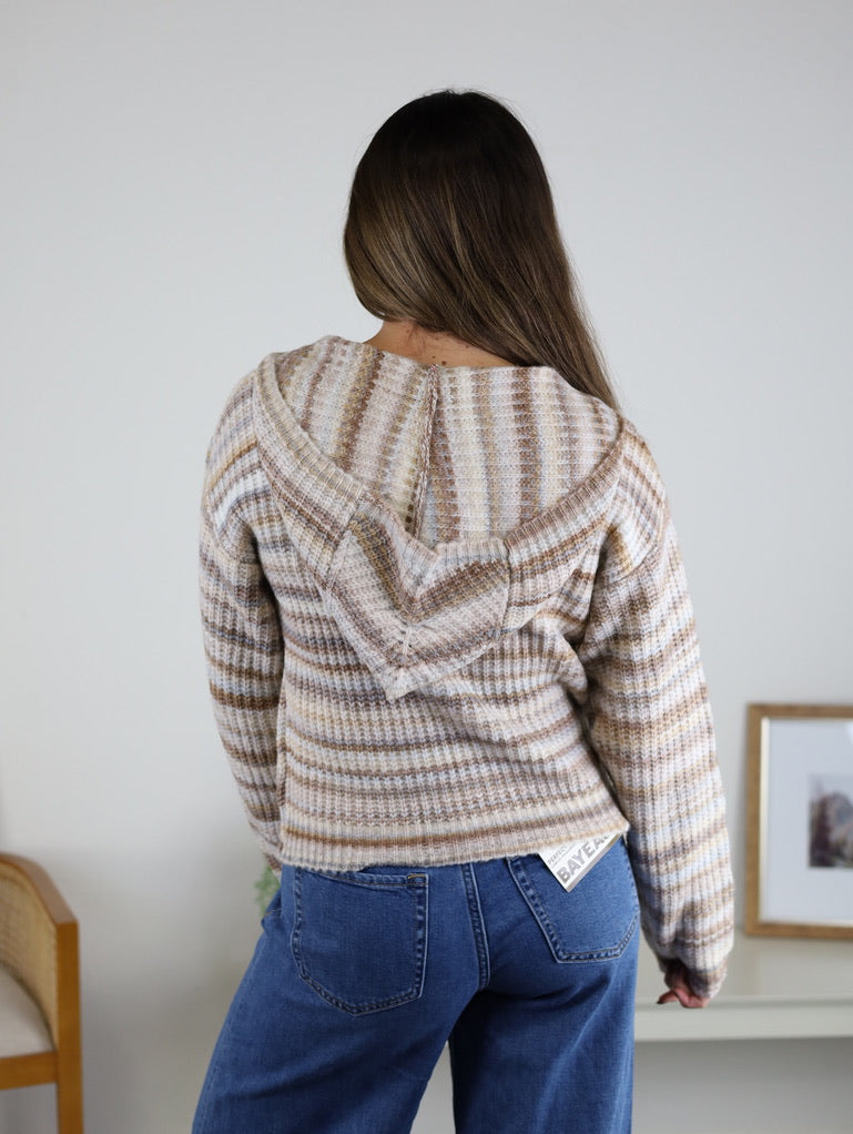 Back view of a person wearing a beige and brown striped Romy Hooded Cardigan Sweater and blue jeans.
