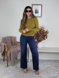 A person wearing a dijon yellow Dee Ribbed Round Neck Tee, dark wash wide-leg jeans, and tan heeled sandals.