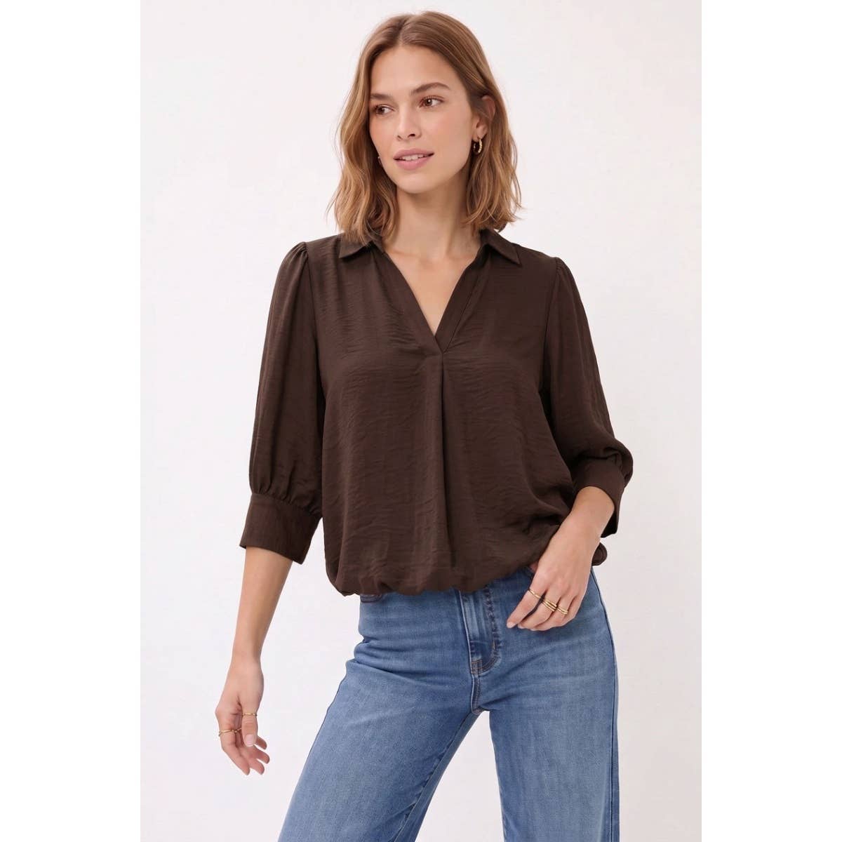A woman wearing a dark brown Naked Zebra - Half Sleeve Hi-lo Bubble Hem Blouse: Wine / L with a v-neck tucked into blue jeans.