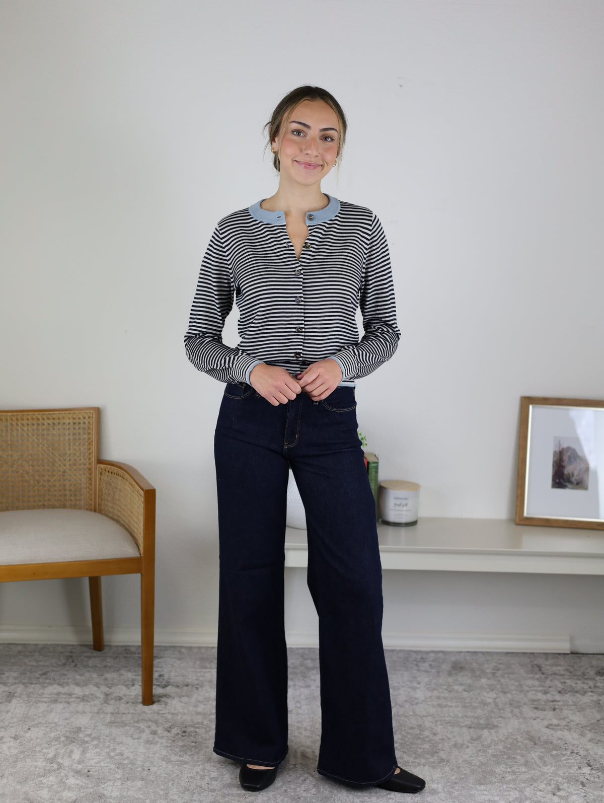 A woman wearing a Vera Striped Cardigan in black-and-white with a light blue collar and dark wash wide-leg jeans.