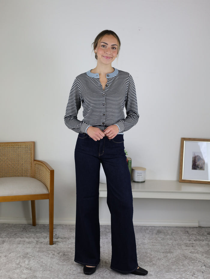 A woman wearing a Vera Striped Cardigan in black-and-white with a light blue collar and dark wash wide-leg jeans.