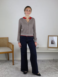 A person wears a Vera Striped Cardigan in brown and white horizontal stripes with red trim and buttons, paired with dark wash wide-leg jeans.