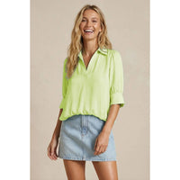 Smiling woman wearing a lime green Naked Zebra - Half Sleeve Hi-lo Bubble Hem Blouse with a collared V-neck and a light-wash denim mini skirt.