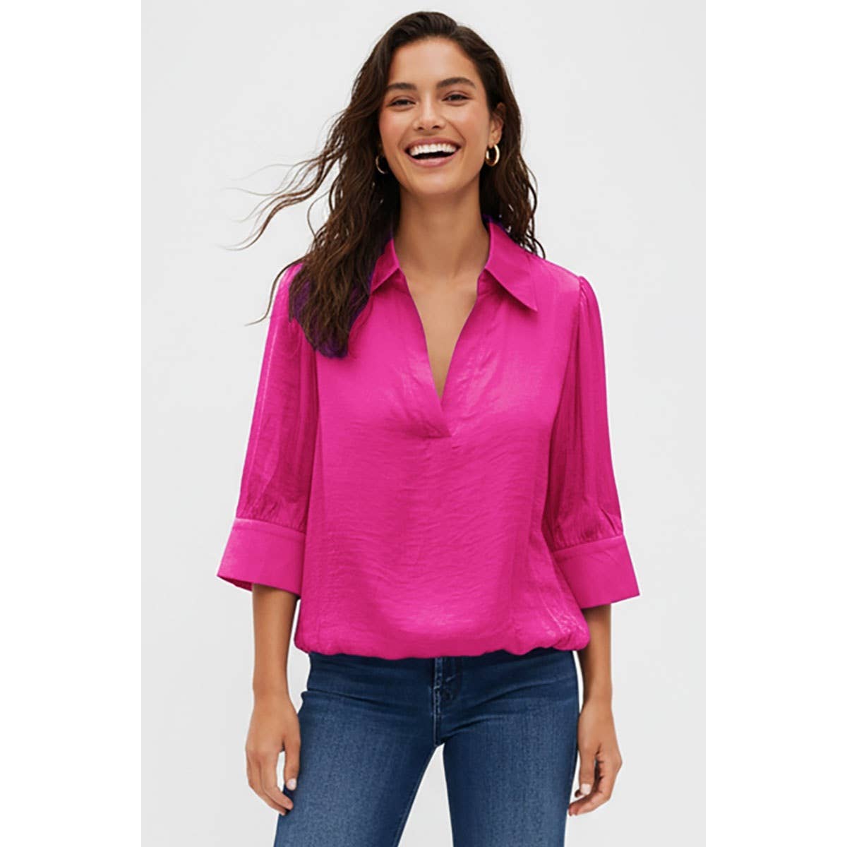 A woman wears a bright pink, half-sleeve V-neck Naked Zebra - Half Sleeve Hi-lo Bubble Hem Blouse: Wine / L and blue jeans.