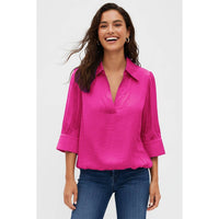 A woman wears a bright pink, half-sleeve V-neck Naked Zebra - Half Sleeve Hi-lo Bubble Hem Blouse: Wine / L and blue jeans.