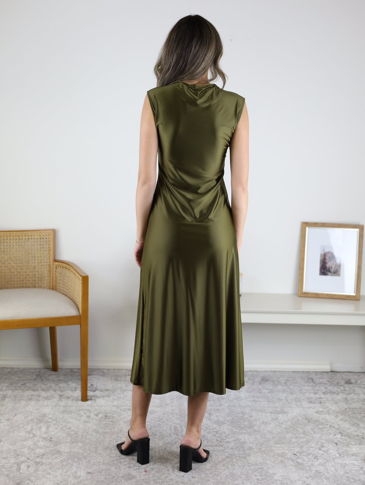A person viewed from behind wearing a Desi Drape Neckline Maxi Dress in olive green with a draped neckline and black heeled sandals.