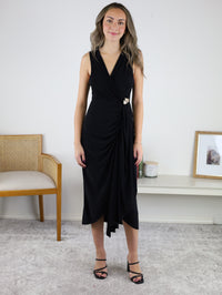 A woman wears the black Kamden Side Gather Midi Dress, a sleeveless V-neck style featuring a side-gathered waist with decorative embellishment and an asymmetrical hemline.