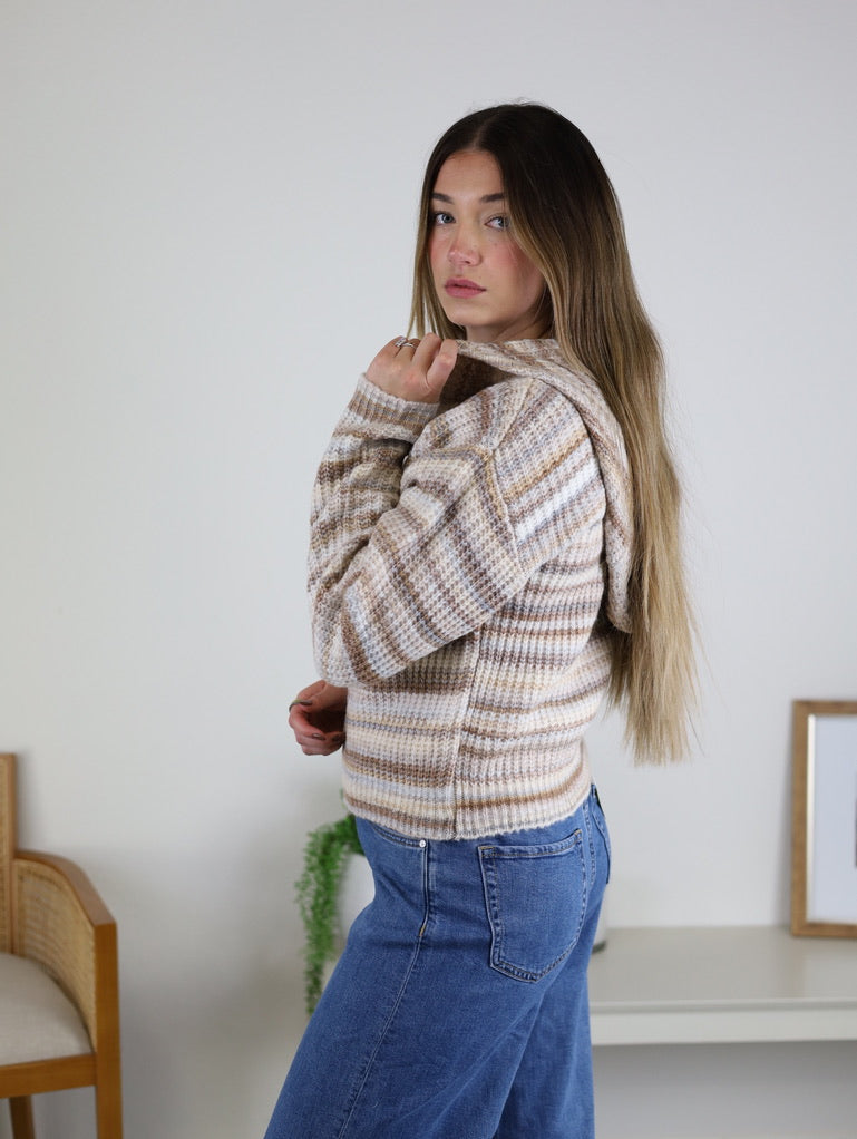 A person wearing a cozy knit striped Romy Hooded Cardigan Sweater and blue jeans.