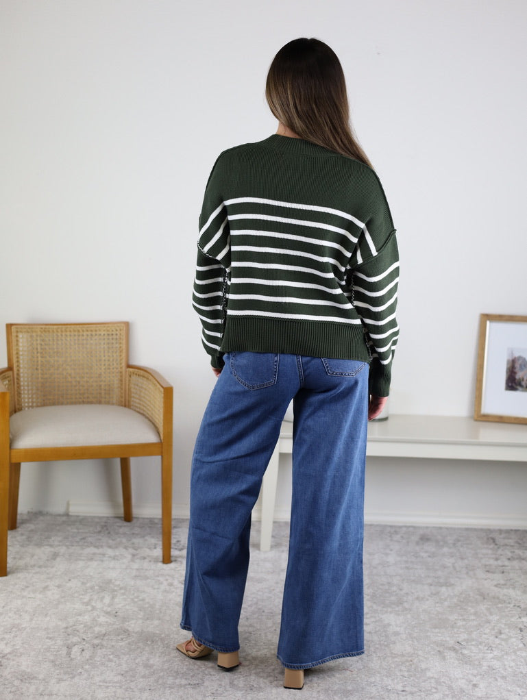 Back view of a person wearing a dark green and white oversized Noa Striped Sweater in cotton knit paired with blue wide-leg jeans.