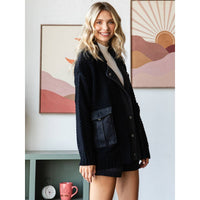 A smiling woman indoors wears the Veveret - Knit Body Denim Layerd Jacket: Cream / Denim / L. Colorful abstract mountain art prints, a pink mug, and decor are visible on a green shelf behind her.