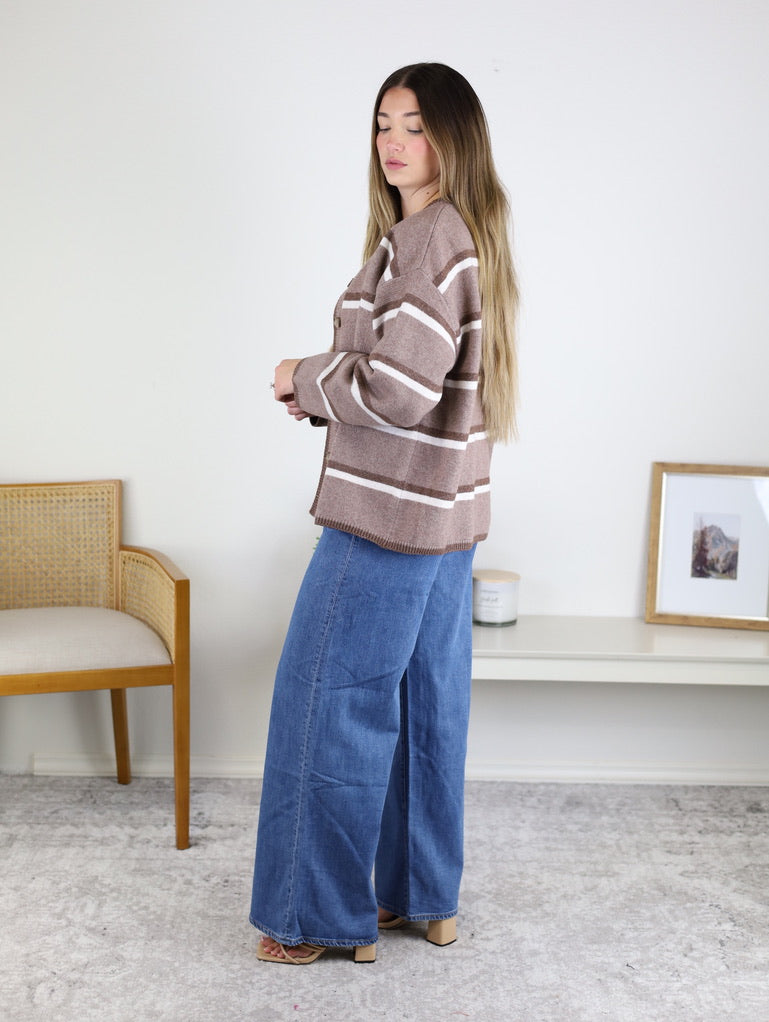 A woman wears a brown and white Nora Stripe Button Down Knit Cardigan paired with relaxed fit blue jeans.