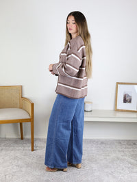 A woman wears a brown and white Nora Stripe Button Down Knit Cardigan paired with relaxed fit blue jeans.