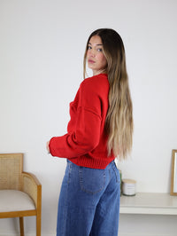 A person wearing a bright red Jude Raw Edge Cardigan and blue jeans.