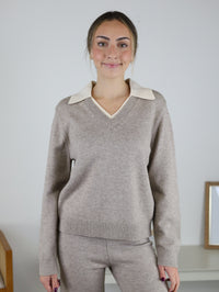 A person wearing a beige Rebecca Sweater/Pant Set featuring a v-neck sweater with a cream collared insert and coordinating knit pants.