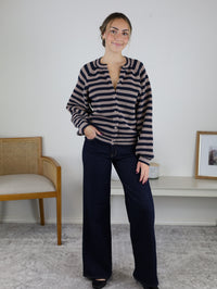 A woman wearing a brown and navy blue striped Justine Longsleeve Crewneck Striped Sweater with long sleeves, a button front, and wide-leg dark wash jeans.