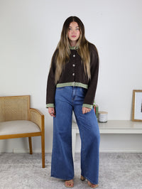A person wears a brown, boxy fit Maya Contrast Hem Cardigan with light green trim at the hem and cuffs, paired with wide-leg blue jeans.