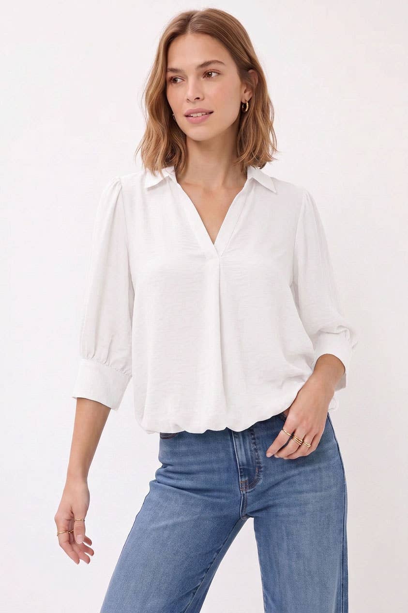A woman wearing a white Naked Zebra - Half Sleeve Hi-lo Bubble Hem Blouse tucked into blue jeans.