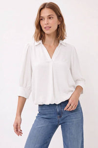 A woman wearing a white Naked Zebra - Half Sleeve Hi-lo Bubble Hem Blouse tucked into blue jeans.