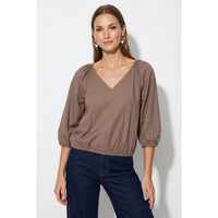 A woman wearing a Naked Zebra - Elastic Puff Sleeve V-neck Blouse: Burgundy / L, featuring three-quarter length puff sleeves and an elasticized waist, paired with dark blue jeans.