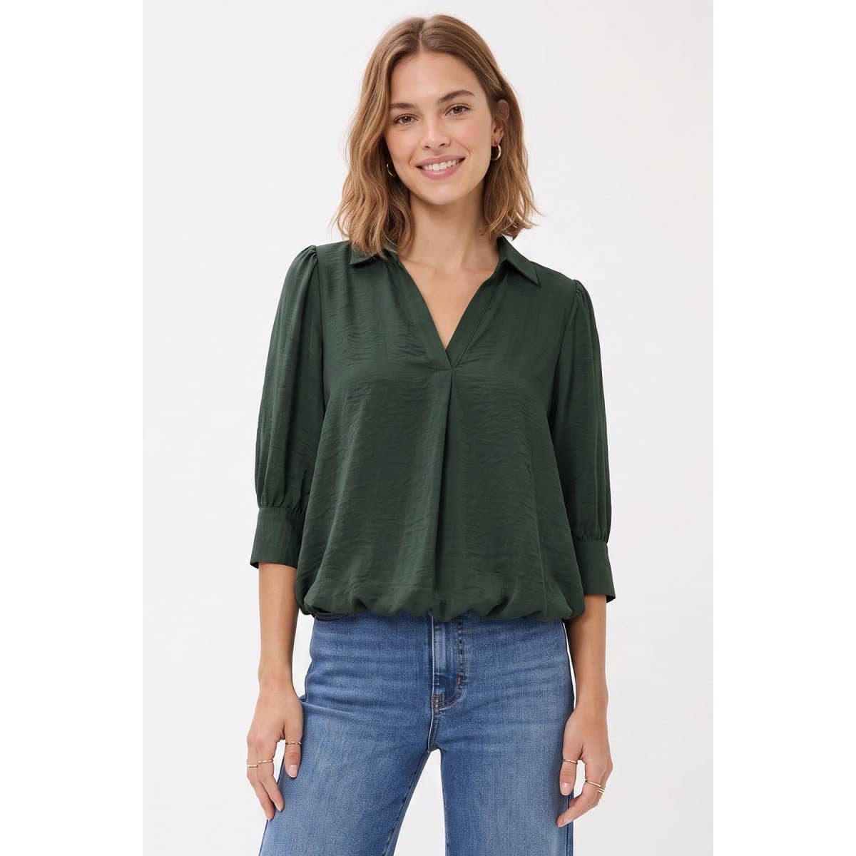 A woman wearing a Naked Zebra - Half Sleeve Hi-lo Bubble Hem Blouse: Wine / L in dark green, featuring a collared V-neck and a bubble hem, paired with blue jeans.