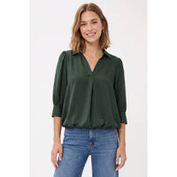 A woman wearing a Naked Zebra - Half Sleeve Hi-lo Bubble Hem Blouse: Wine / L in dark green, featuring a collared V-neck and a bubble hem, paired with blue jeans.