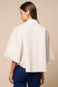 Woman wearing a cream-colored, short-sleeved Jordan Fur Cape Sleeve Jacket over dark blue jeans.