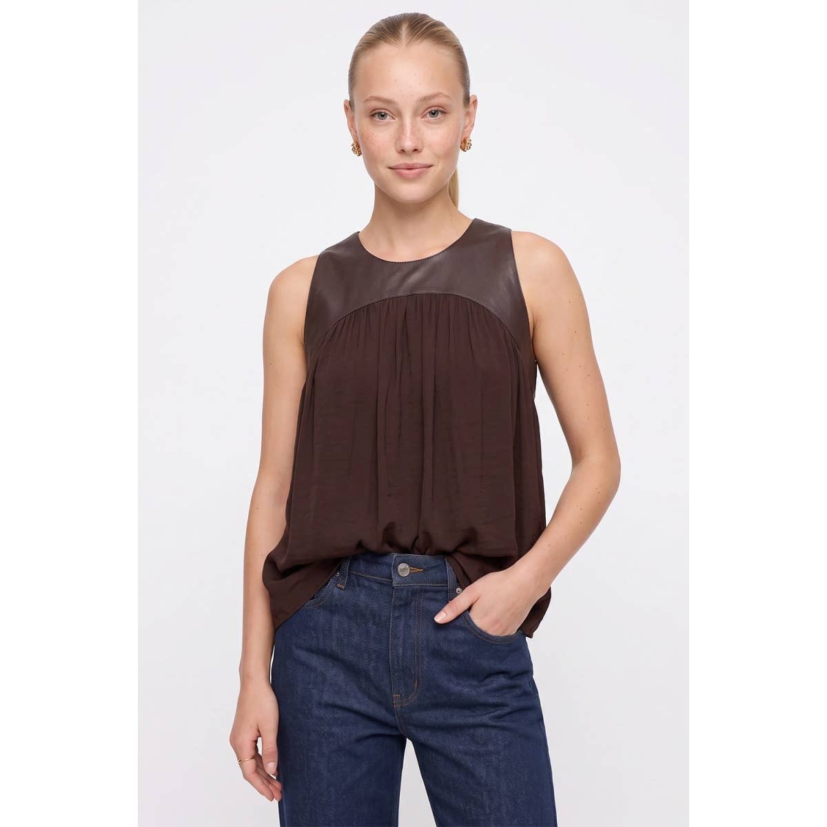 A woman wears a Naked Zebra - Vegan Leather Yoke Satin Tank in wine, featuring a solid chest panel and a gathered bodice, paired with blue jeans.
