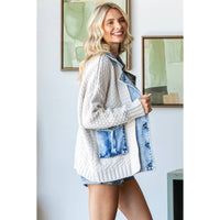 Smiling woman with long blonde hair wears a Veveret - Knit Body Denim Layerd Jacket: Cream / Denim / L and shorts, standing indoors near abstract art on a white wall.