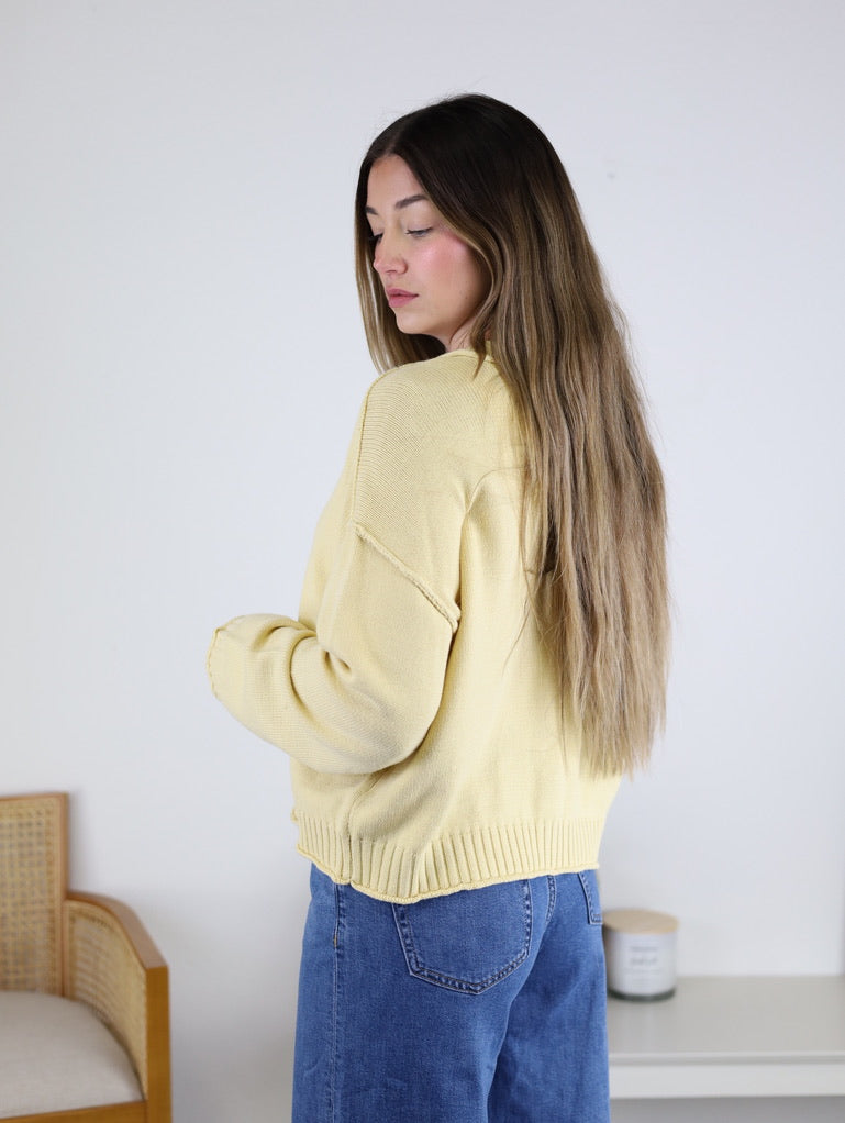 A person wearing a pale yellow, long-sleeved Jude Raw Edge Cardigan with blue jeans.